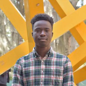 A portrait of a black man standing in front of a yellow abstract structure